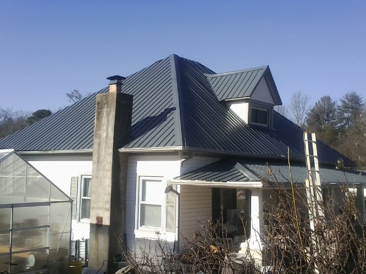 Dark blue standing seam metal roof on a white farmhouse with dormer — Slate & Tile Roof Repair by Roofing Brothers in Vergennes