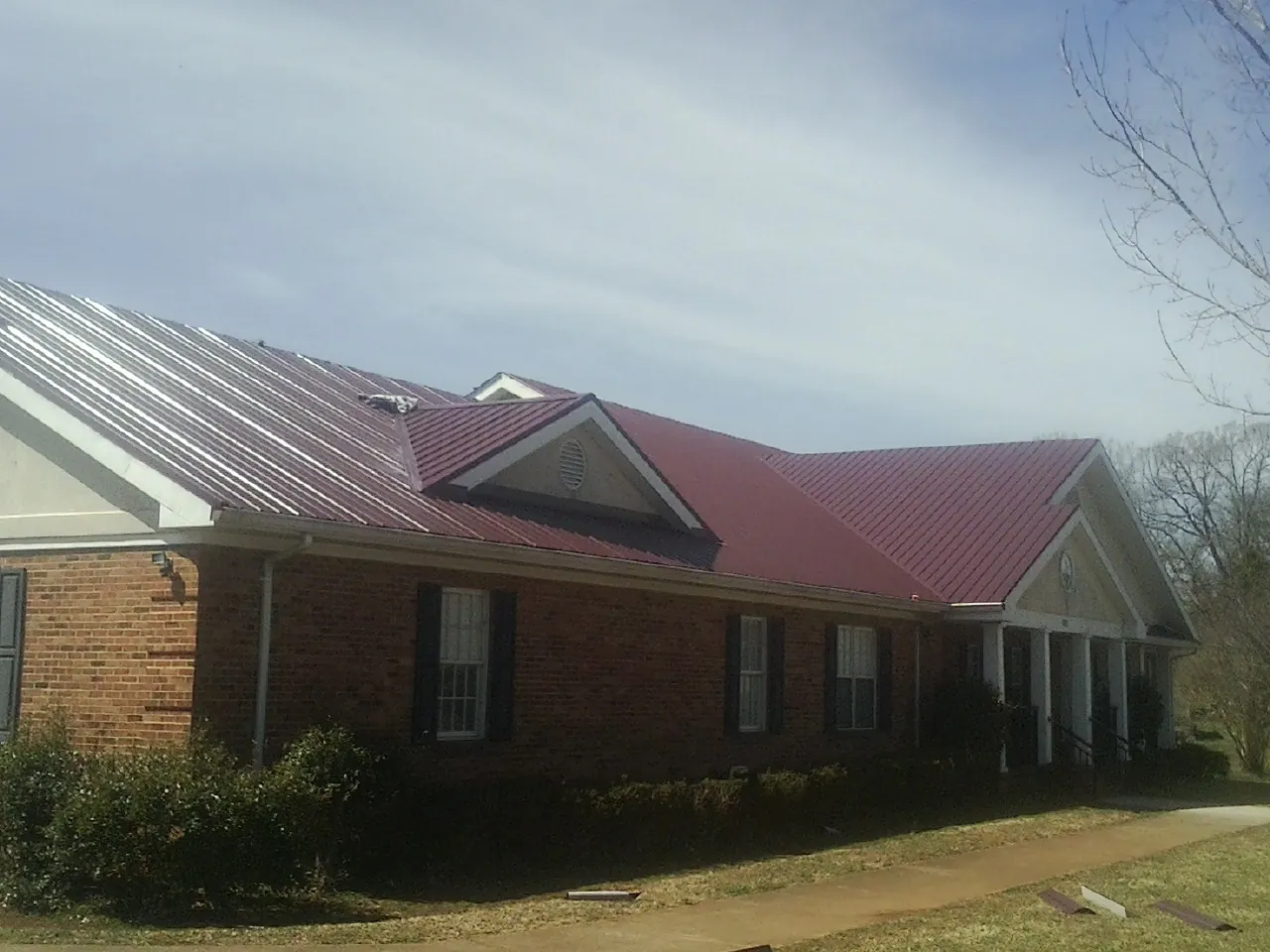 Red metal roof with gabled entries on a long brick building, from a Hail Damage Roof Repair job in Vergennes