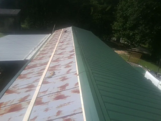 Old rusted panels beside newly installed green metal roofing — Wind Damage Roof Repair by Roofing Brothers in Vergennes