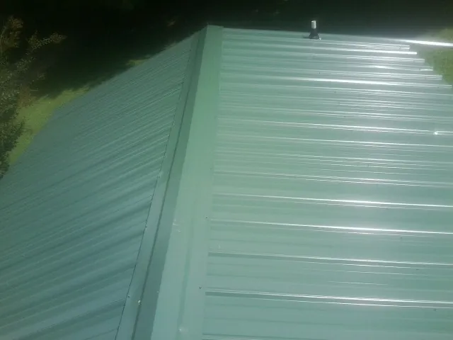 New green metal panels meeting at the ridge of a roof — Flat Roof Repair work by our crew in Vergennes