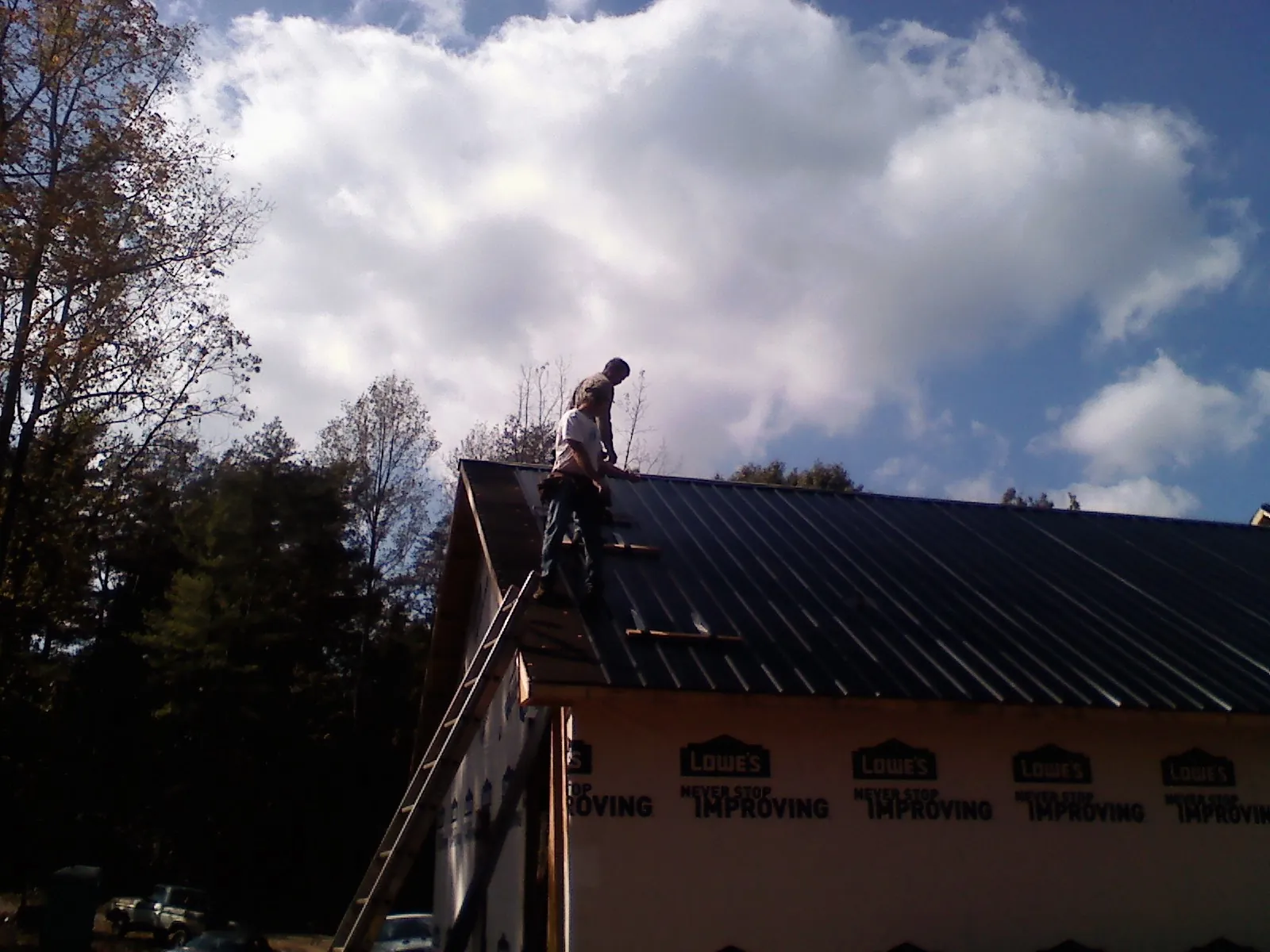 Roofer fastening dark metal panels high against a cloudy sky, from a Roof Inspection job in Vergennes