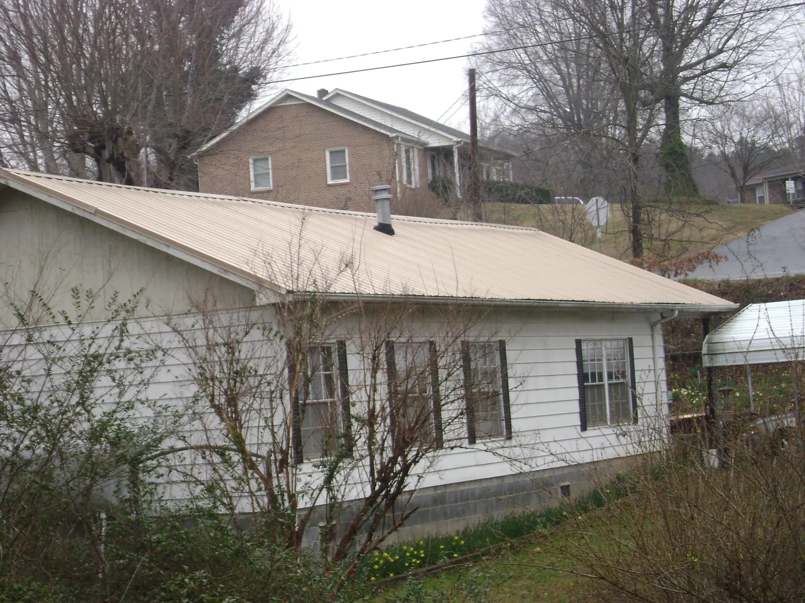 Tan metal roof on a white sided house set into a hillside — Commercial Roofing by Roofing Brothers in Vergennes